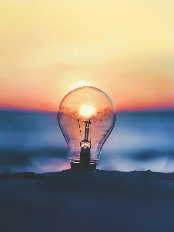 A lightbulb framing the sunset, while set on a beach.