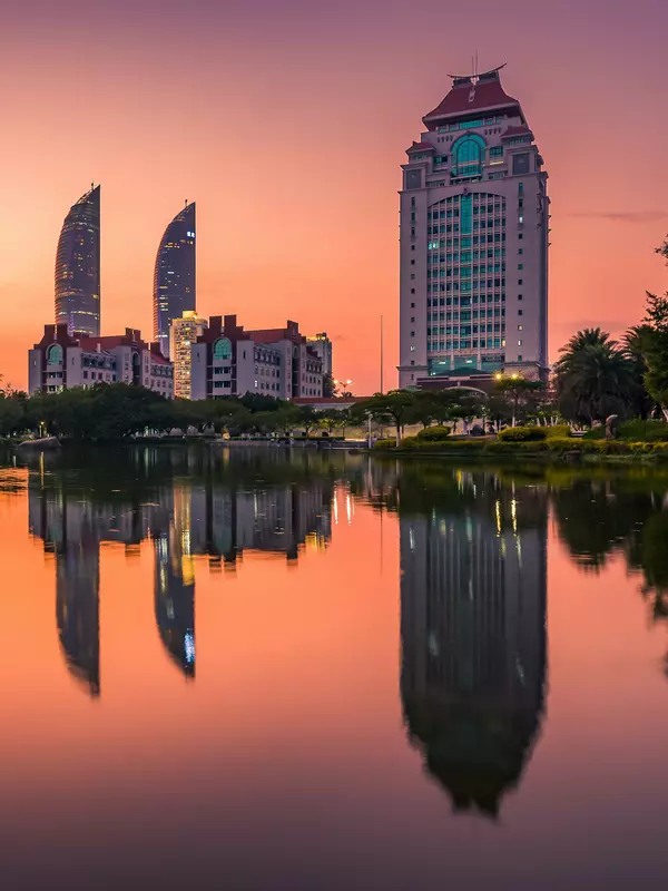 Xiamen University buildings form the skyline at sunset and are reflected in a pool of water