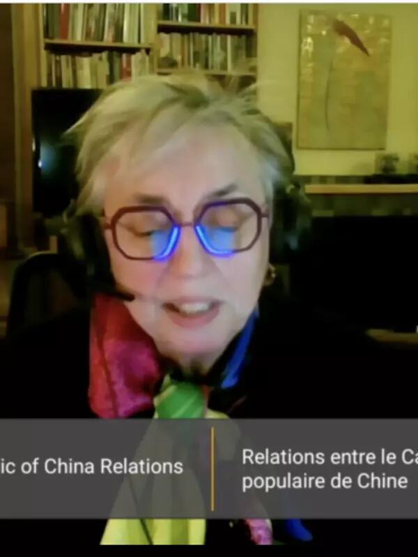Woman sitting and wearing a microphone headset with the screen saying "Canada-People's Republic of China Relations" in English and French 