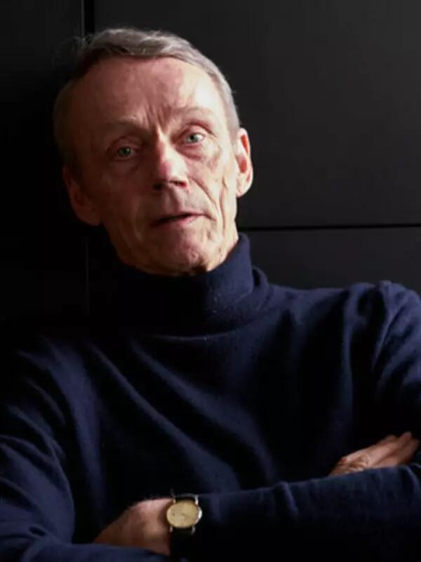 Man wearing a blue turtleneck, sitting with his arms crossed. 