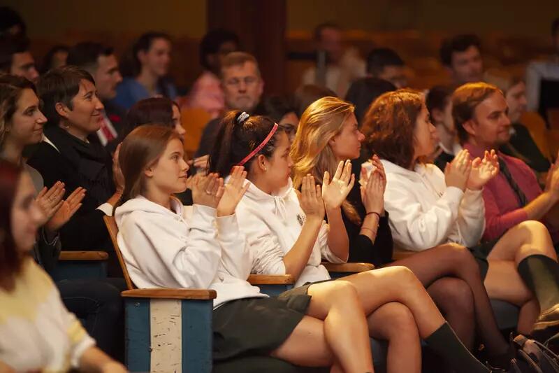 Several rows of students sitting in an auditorium and clapping