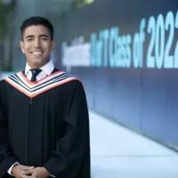 A student in convocation regalia poses for a photo infront of a large U of T Class of 2022 sign
